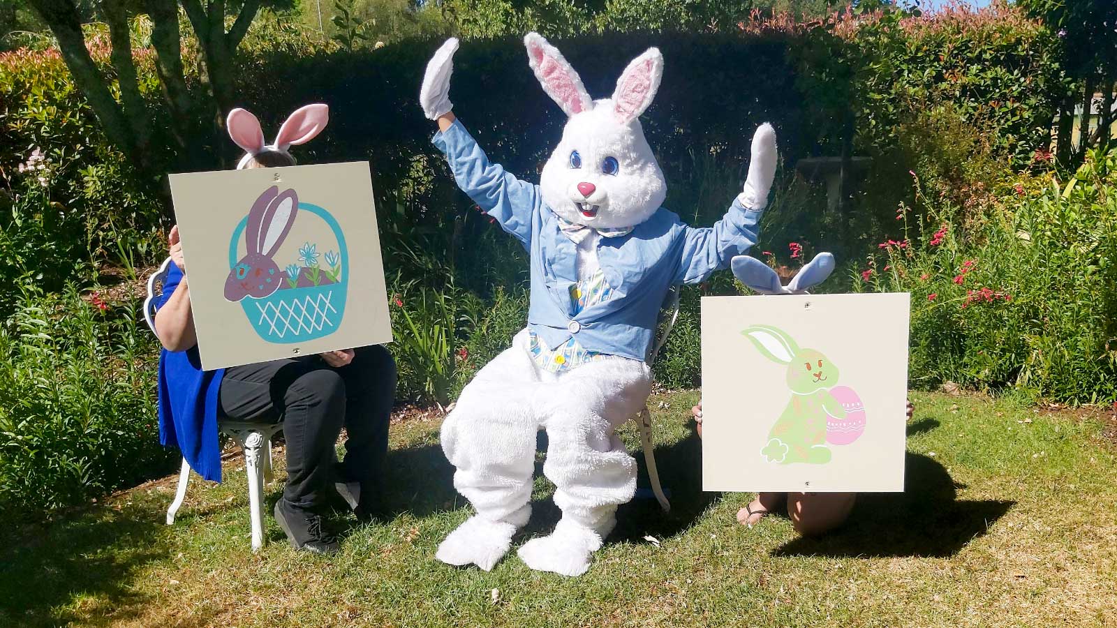 Person in bunny suit with children holding drawings of Easter eggs